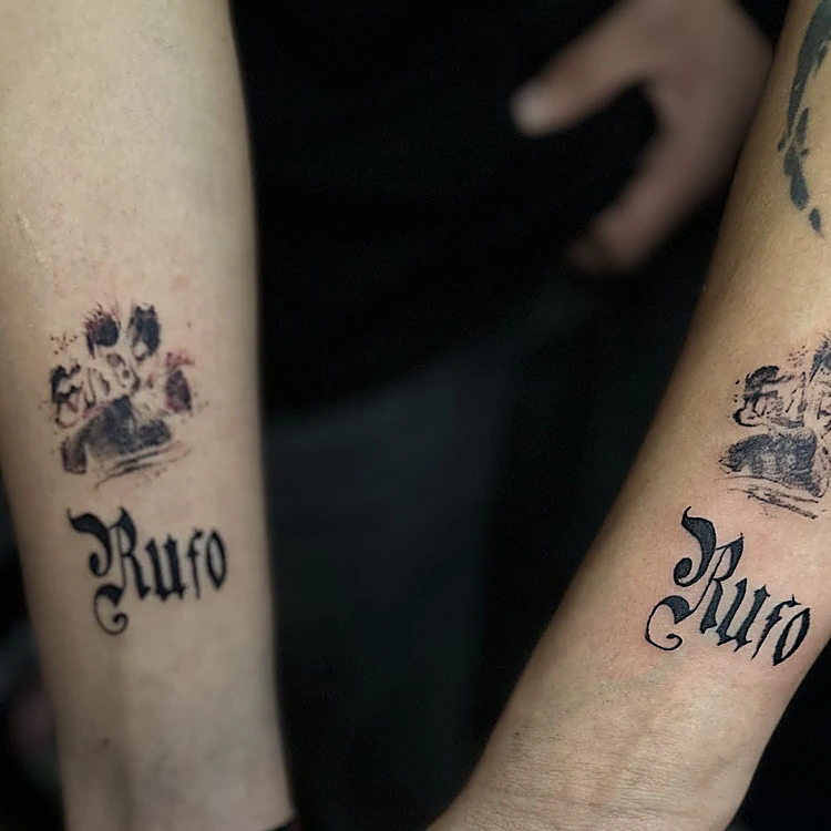 Dos antebrazos con la misma huella de perro y el nombre Rufo en letra gótica.
