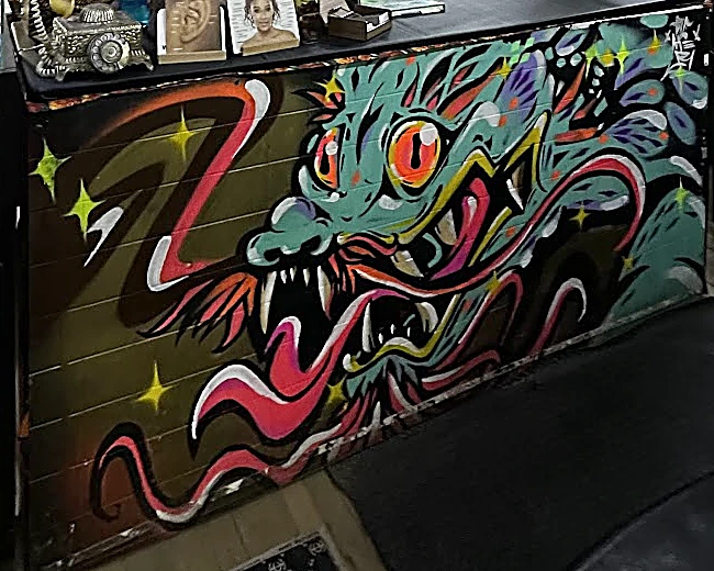 El frente del mostrador pintado con un dragón turquesa de ojos naranjas, lengua rosa y estrellas amarillas.