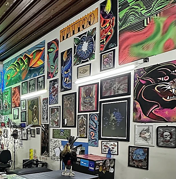 Pared del estudio cubierta de cuadros enmarcados, pinturas fluorescentes y un rótulo naranja que dice Tattoo.