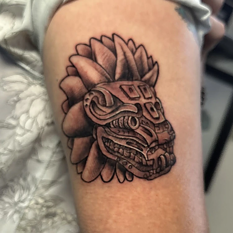 Tatuaje en el brazo: cabeza de serpiente emplumada de estilo prehispánico, en negro y gris.